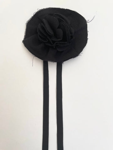 A handmade black flower accessory made with scrap fabric, displayed against a white background.