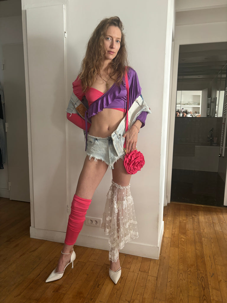 Woman posing in a room wearing a pink and purple top with a pink flower coin purse in her hand.
