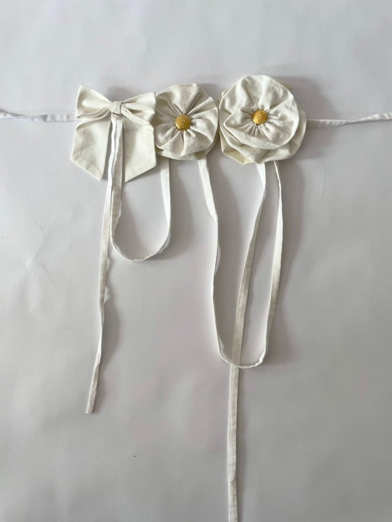 Handmade white flower and bow accessory with gold button centers and long straps by Sarah Aphrodite, made from upcycled fabric scraps, worn as belt or top