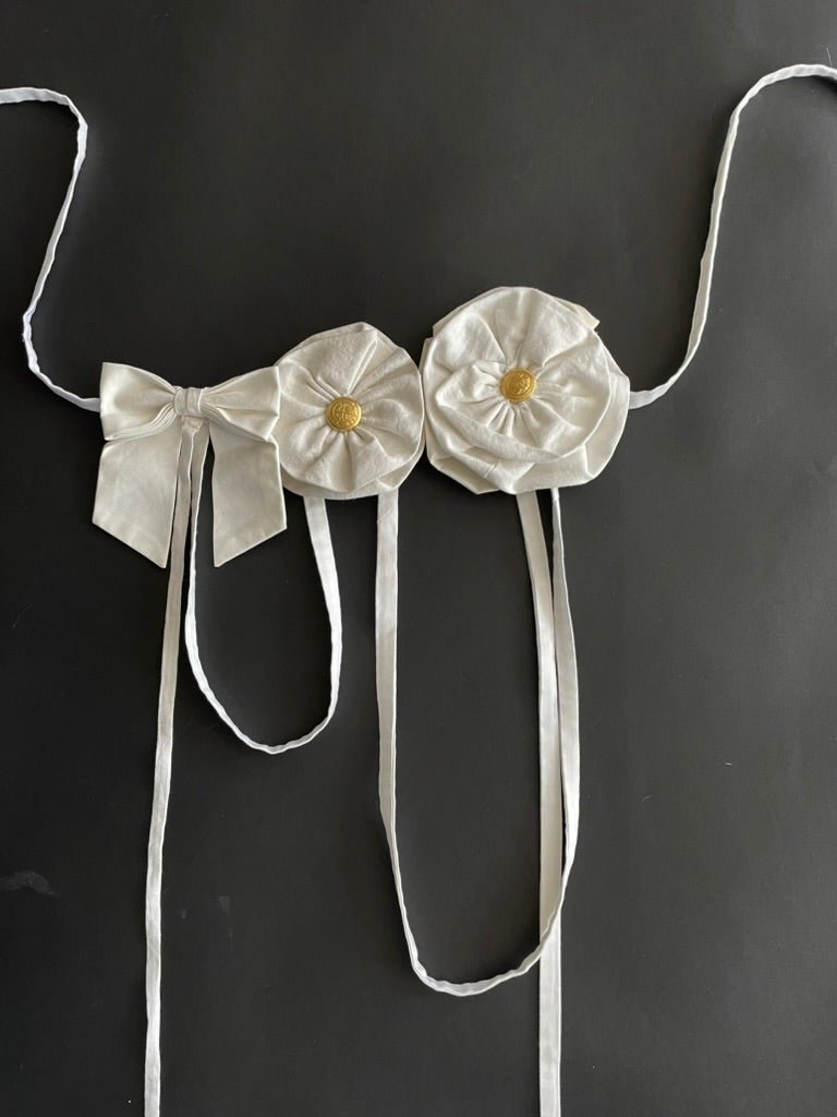 Handmade white flower and bow accessory with gold button centers and long straps by Sarah Aphrodite, made from upcycled fabric scraps, worn as belt or top