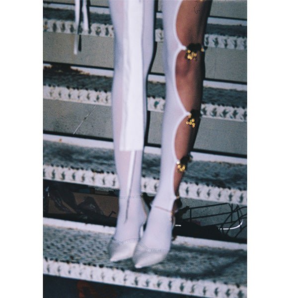 Handmade white opaque tights with seven reused gold elephant buckles along the left leg by Sarah Aphrodite, limited-edition upcycled fashion piece