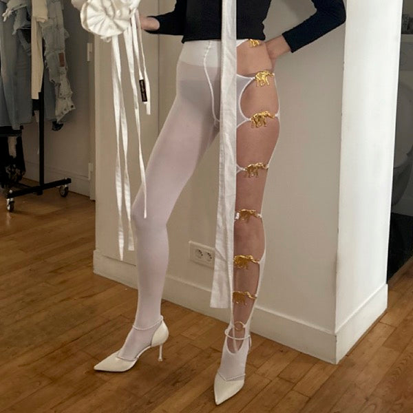 Handmade white opaque tights with seven reused gold elephant buckles along the left leg by Sarah Aphrodite, limited-edition upcycled fashion piece