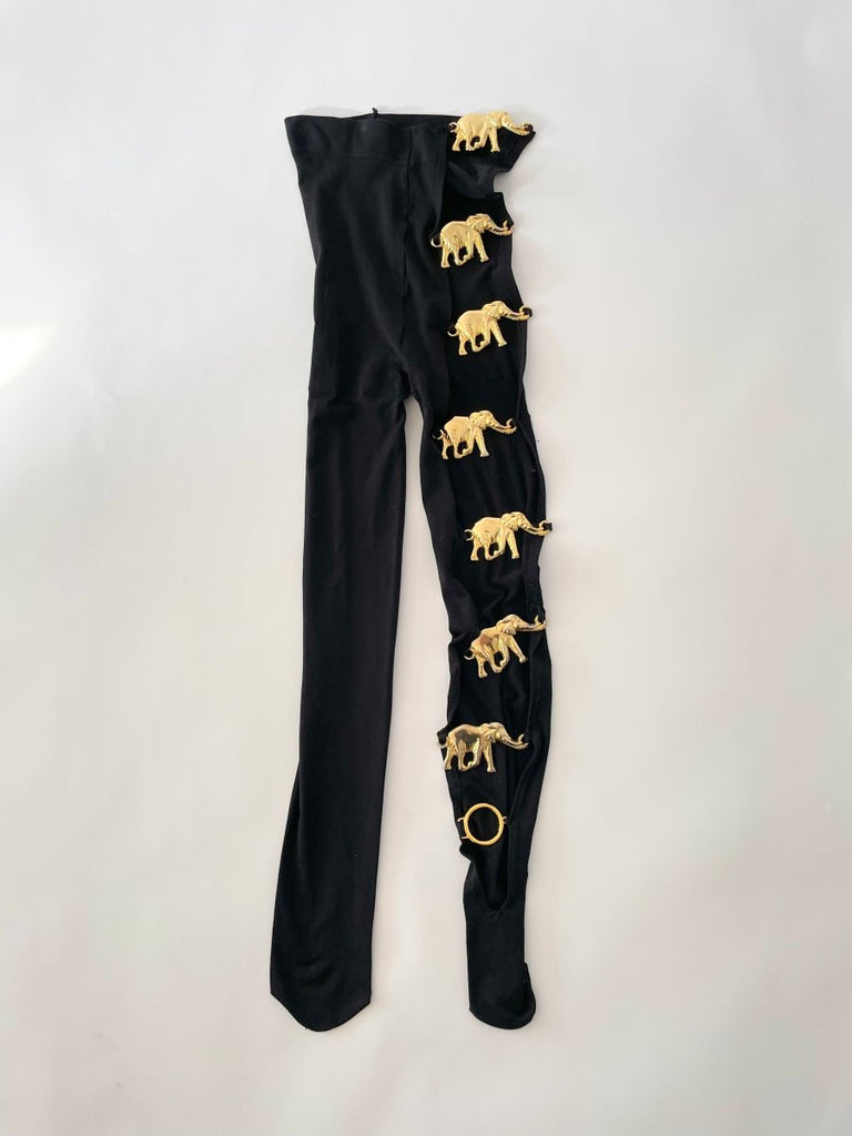 Handmade white opaque tights with seven reused gold elephant buckles along the left leg by Sarah Aphrodite, limited-edition upcycled fashion piece