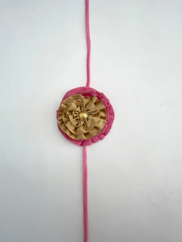Handmade pink and gold double fabric flower accessory with gold button center, shown with elastic ties for wearing on ankle or shoulder.