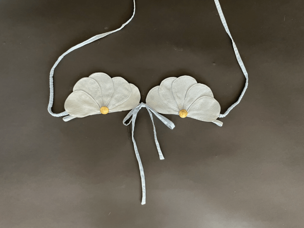 White shell-shaped top accessory with gold buttons on a dark background