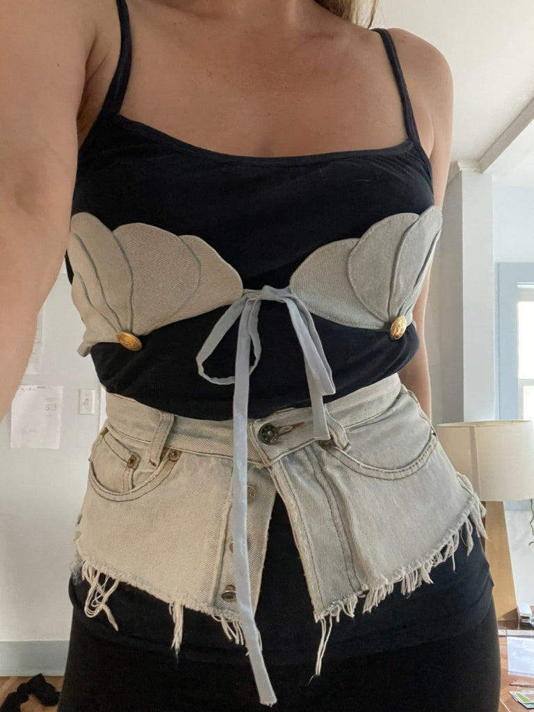 Person wearing a black tank top with a light blue denim scallop bra accessory on top and a matching denim jeans belt 