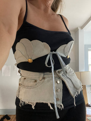 Person wearing a black tank top with a light blue denim scallop bra accessory on top and a denim jeans belt 
