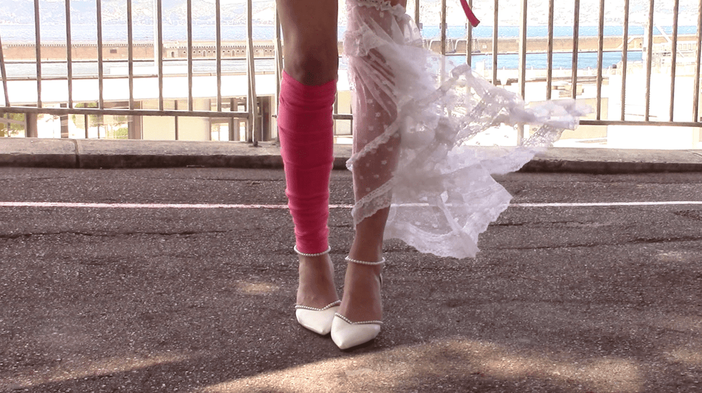 Person wearing pink knee-high legpiece and a white lace legpiece and white shoes on a street with a blurred background