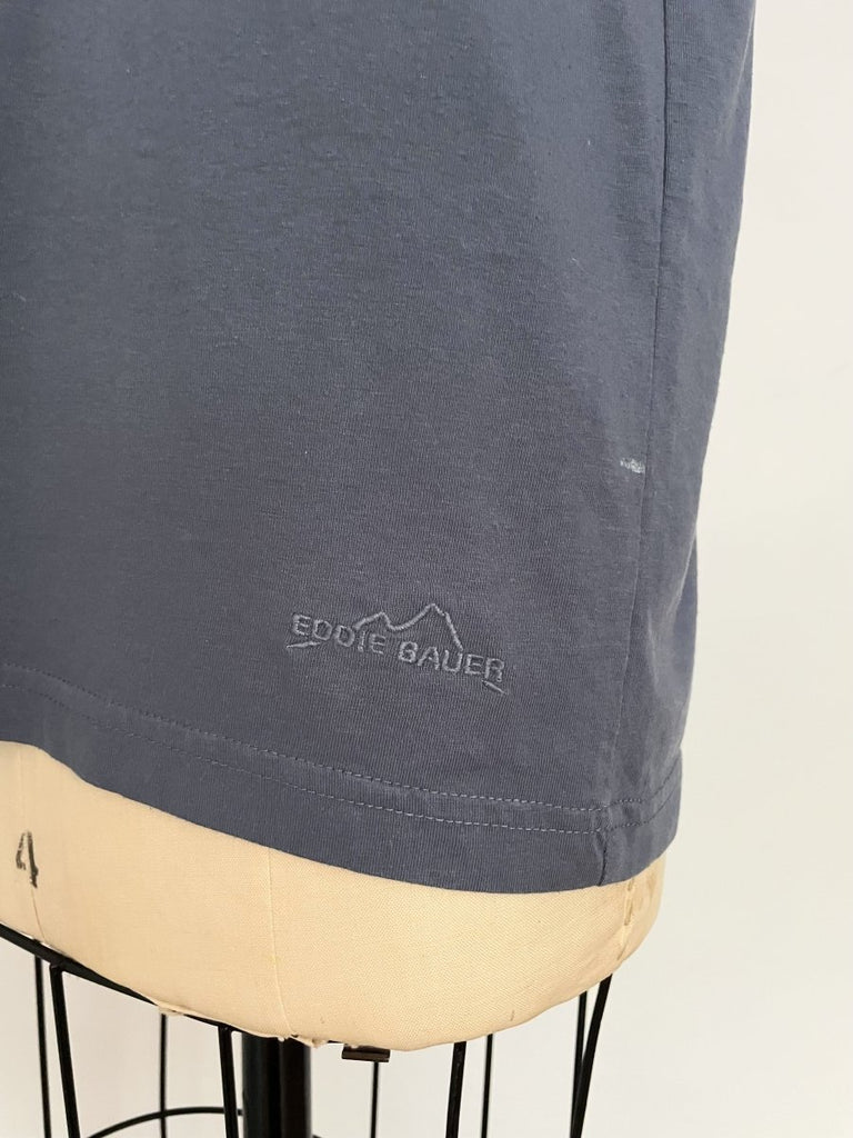 One-of-a-kind sustainable greyish blue t-shirt by Sarah Aphrodite. Large heart cut-out on chest, Eddie Bauer logo on bottom left with paint stain. Fits XS–Large.