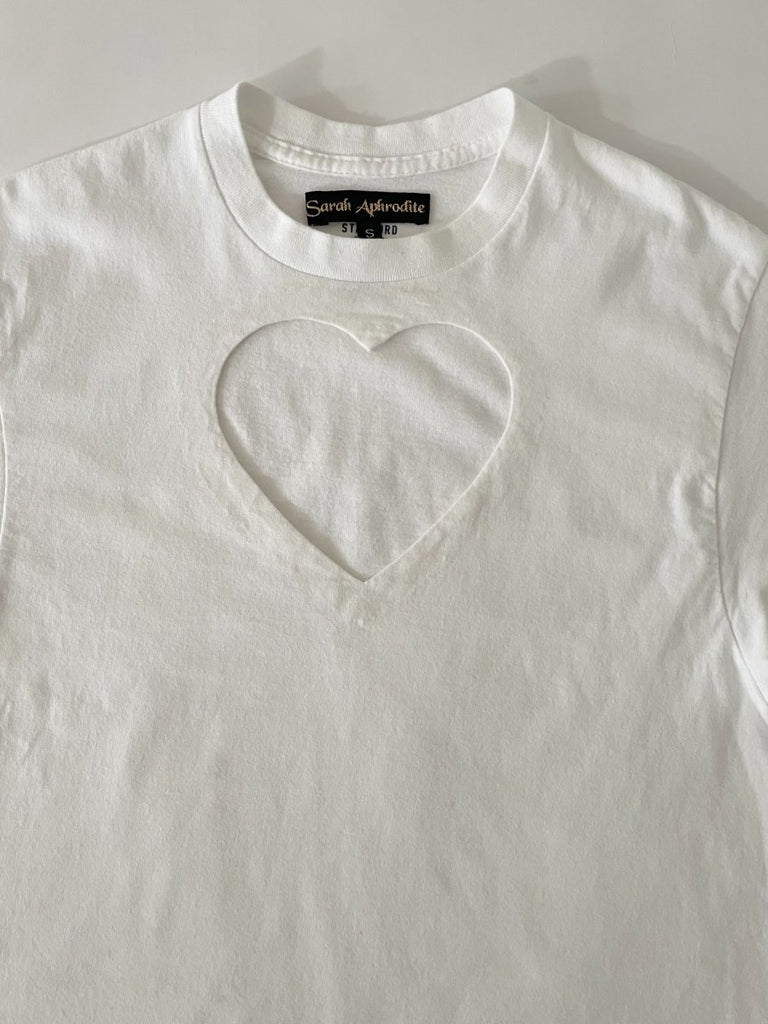 One-of-a-kind sustainable white t-shirt by Sarah Aphrodite, featuring a large heart cut-out. Handmade from repurposed fabric. Fits S–M, eco-conscious design.