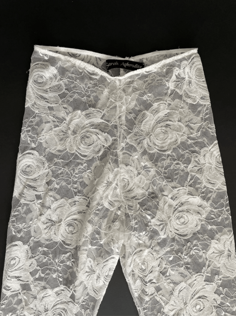 White floral lace leggings with a black Sarah Aphrodite label on the inside of the leggings photographed on a black background