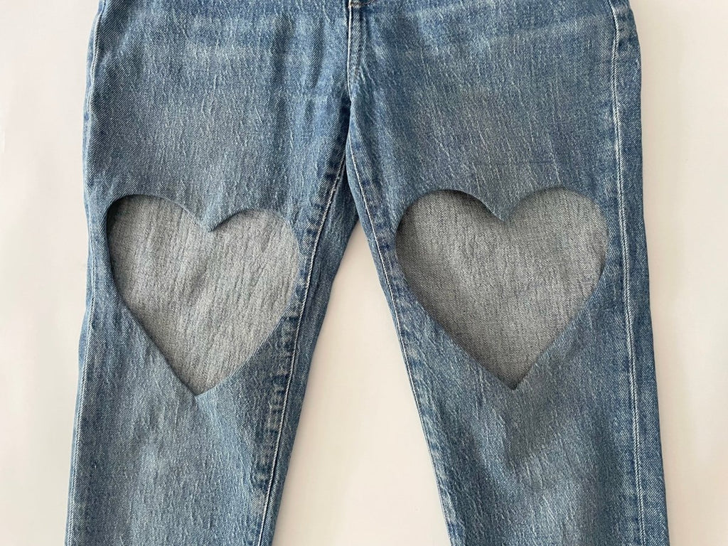 Blue jeans close up on of a  heart cut out on each leg on a white background