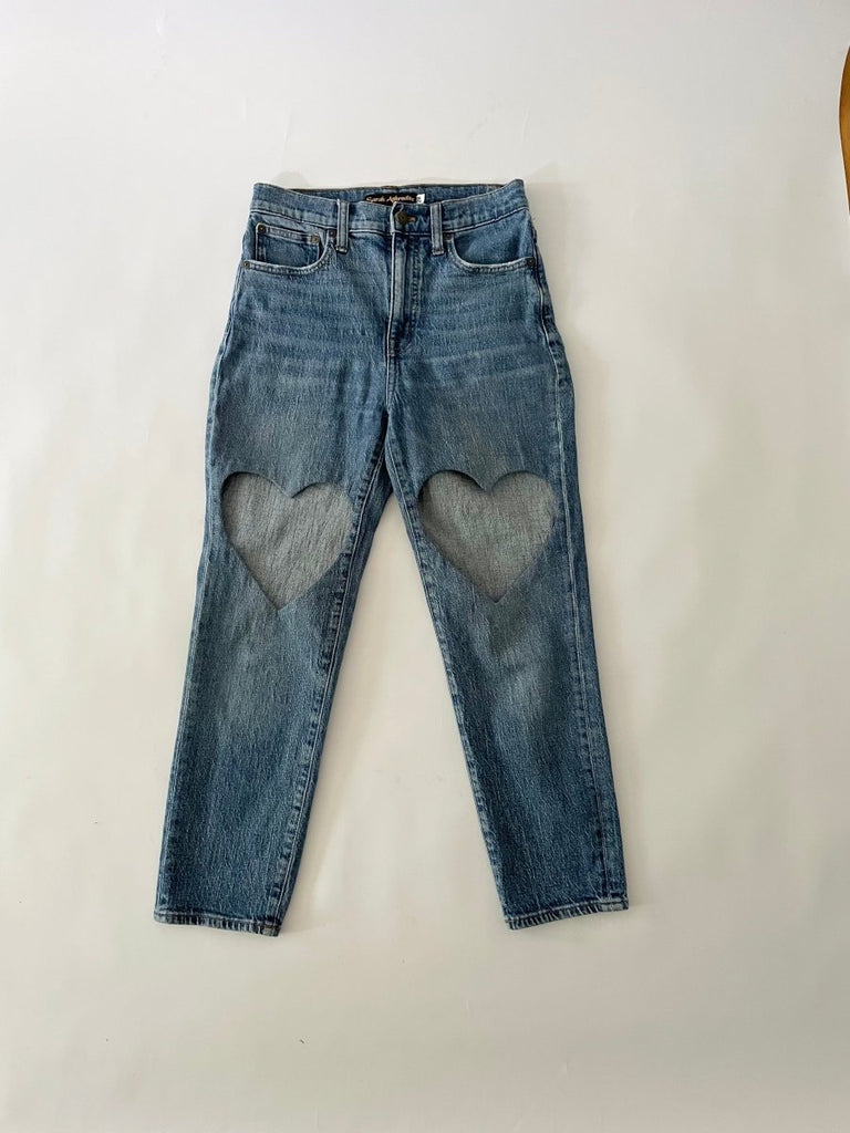 Blue pair of jeans with a heart cut out on each leg on a white background