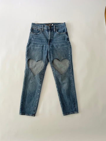 Blue pair of jeans with a heart cut out on each leg on a white background