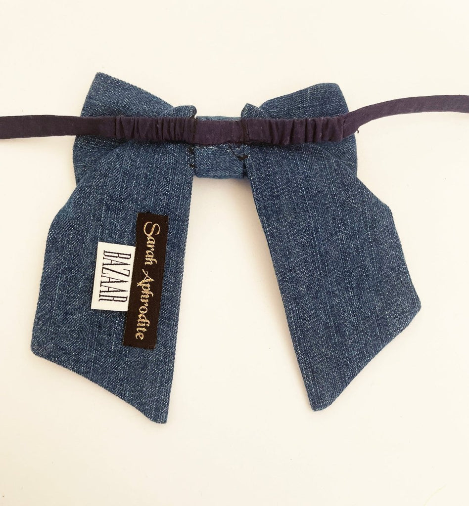 back of a medium-sized denim bow accessory with fabric ties and a Sarah Aphrodite label, handmade from upcycled denim, displayed against a white background