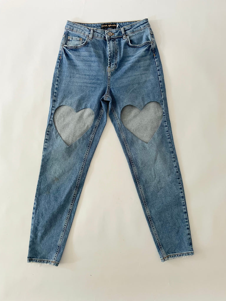 Blue jeans with heart-shaped cut outs on a white background