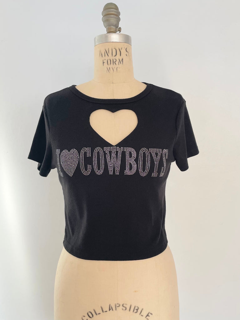 A black crop top t-shirt with a heart cut-out design and 'I LOVE COWBOYS' print in rhinestones, displayed on a mannequin.