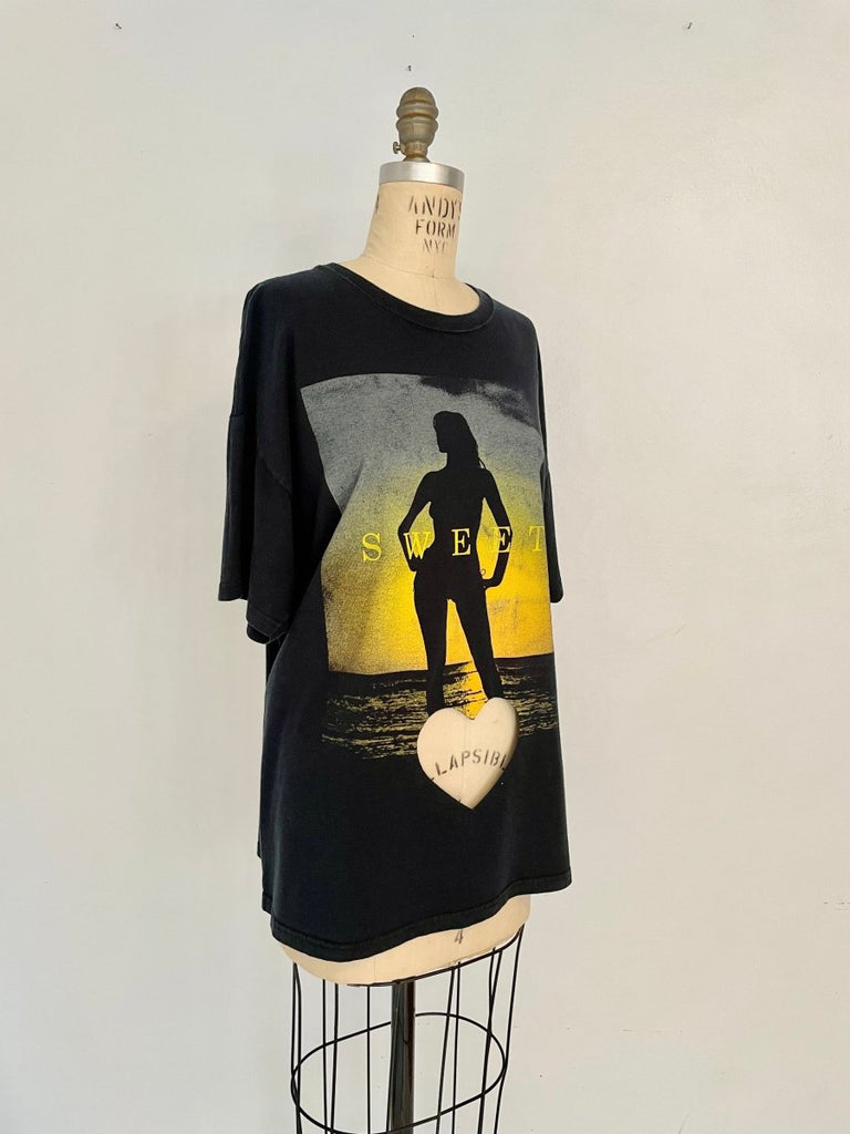 An oversized black t-shirt with a heart cut-out design on the belly featuring a female figure standing in the sea