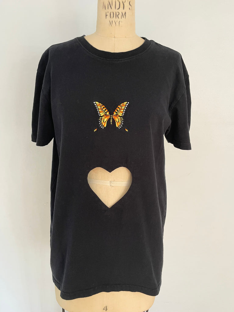 A black T-shirt with a heart cut out and an embroidered butterfly on the front, displayed on a mannequin.