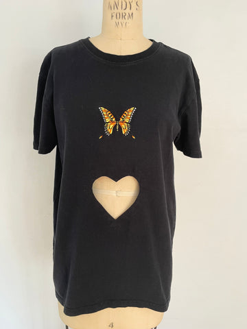 A black T-shirt with a heart cut out and an embroidered butterfly on the front, displayed on a mannequin.