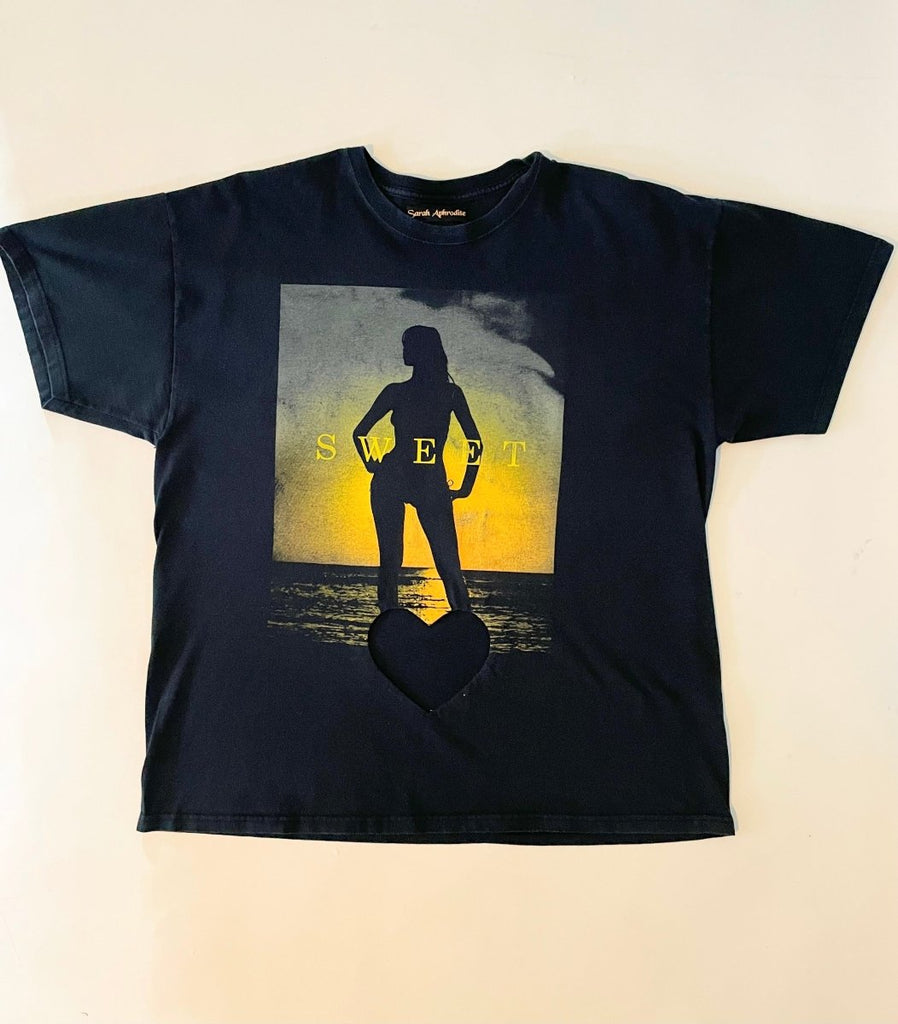 An oversized black t-shirt with a heart cut-out design featuring a female figure, displayed flat on the floor