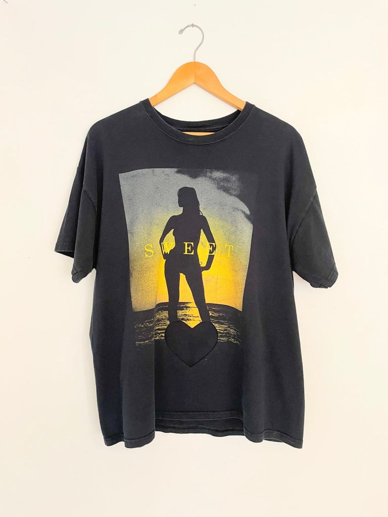 An oversized black t-shirt with a heart cut-out design featuring a female figure, displayed on a hanger