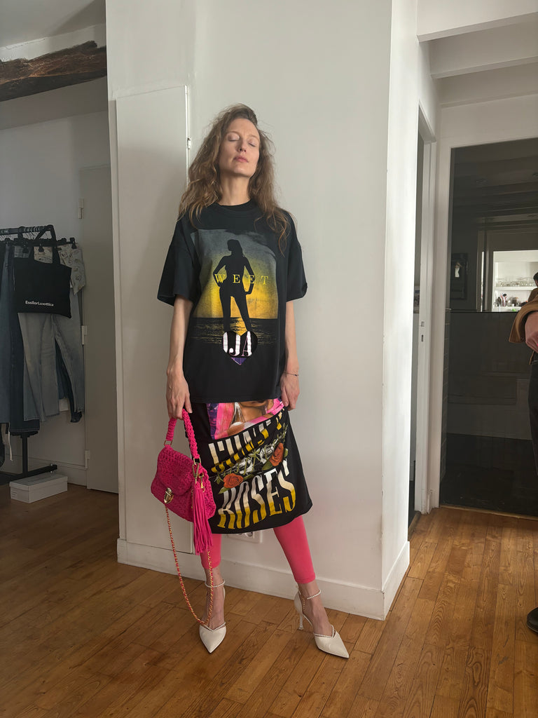 Woman wearing a black graphic t-shirt and pink leg pieces standing in a room with wooden flooring.