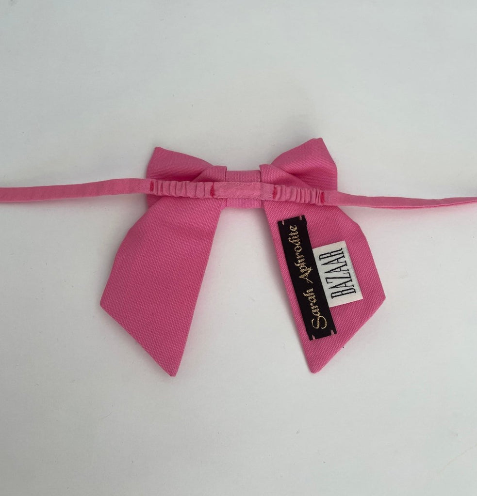 Small bow accessory in light pink fabric with elastic ties, displayed against a white background