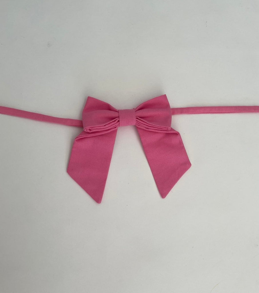 Small bow accessory in light pink fabric with ties, displayed against a white background