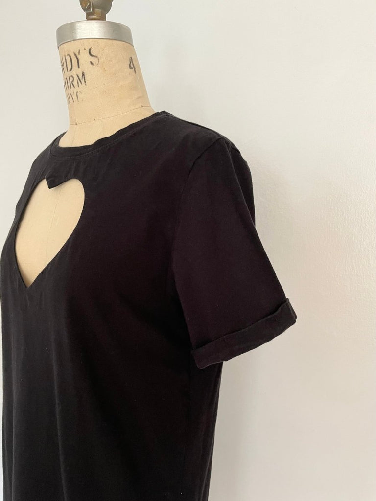 A black t-shirt mini dress with a rolled up sleeve and a large heart cut out on the chest displayed on a mannequin.