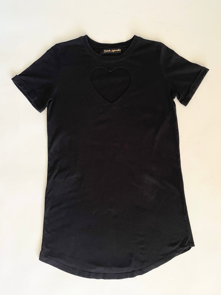 A black t-shirt with a heart cut-out on the chest  displayed flat on the floor on a white background.
