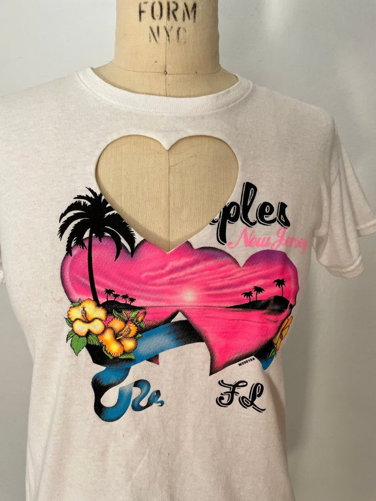 A white vintage-style heart cut out t-shirt and a heart print and text graphic on the front, displayed on a mannequin.