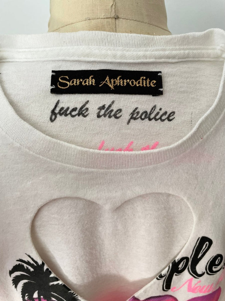 A white vintage-style heart cut out t-shirt and and a fuck the police print on the inside of the shirt and a Sarah Aphrodite label, displayed on a mannequin.