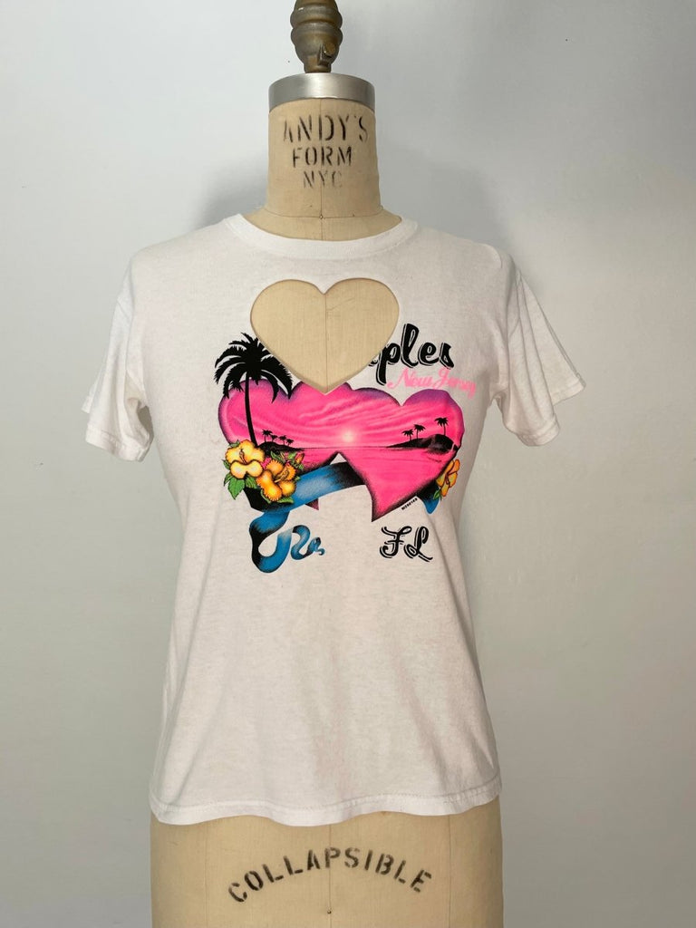 A white vintage-style heart cut out t-shirt and a heart print and text graphic on the front, displayed on a mannequin.