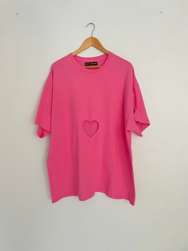 Oversized pink t-shirt with a heart cut-out in the center, displayed on a hanger