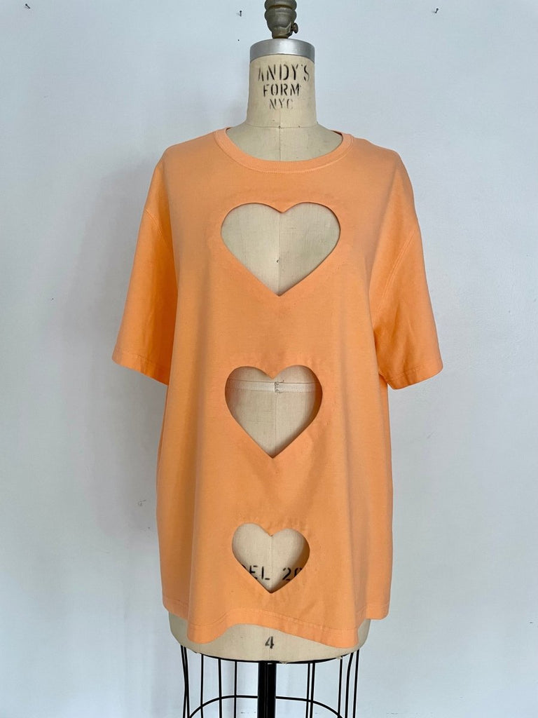 Peach t-shirt with three heart cut-outs displayed on a mannequin against a white background