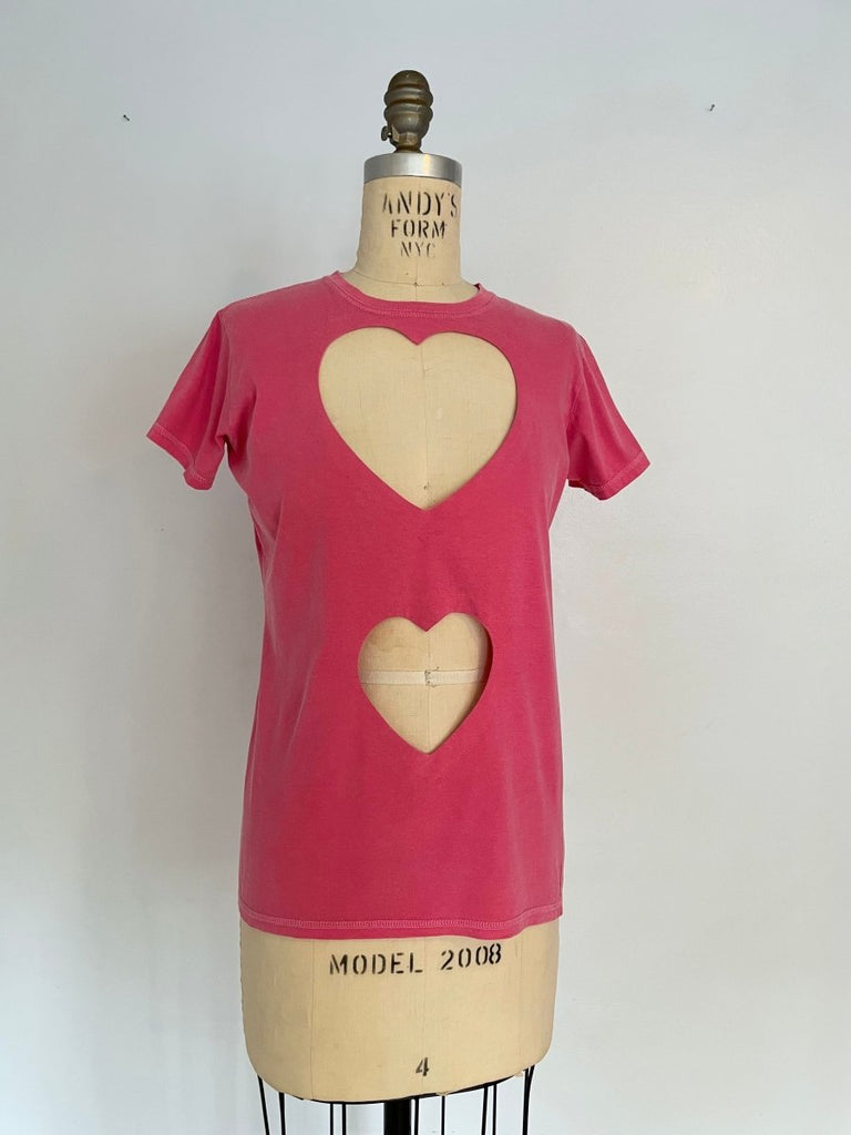 A pink fitted double heart cut-out T-shirt on a mannequin, showcasing the front view with a visible heart-shaped cut-out on the chest  and belly area.