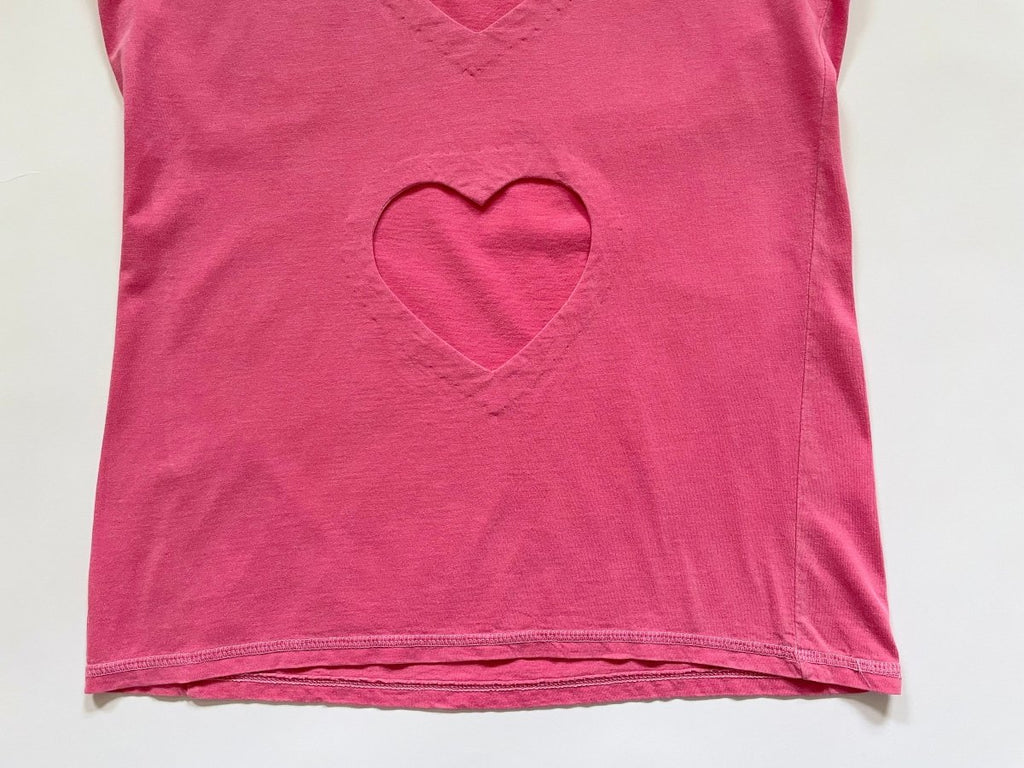 a close up of a heart cut out and a twisted side seam on a pink repurposed T-shirt displayed flat on a white background