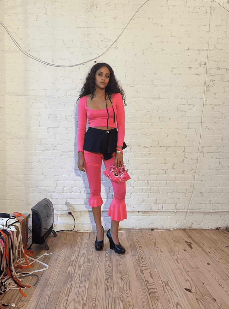 model wearing a bright pink outfit with asymmetrical ruffle leggings and matching pink long sleeve top and a Sarah Aphrodite one of a kind pink handbag.