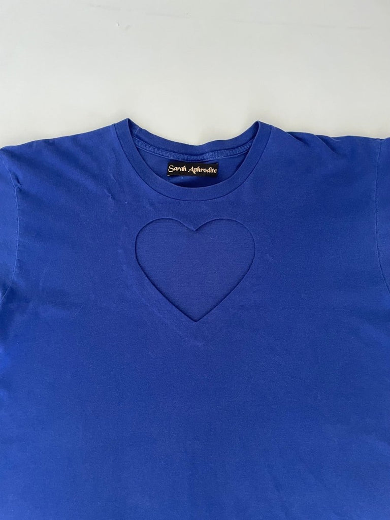 detail of a Ultramarine blue t-shirt with a heart cut-out design in the center, displayed flat on the floor