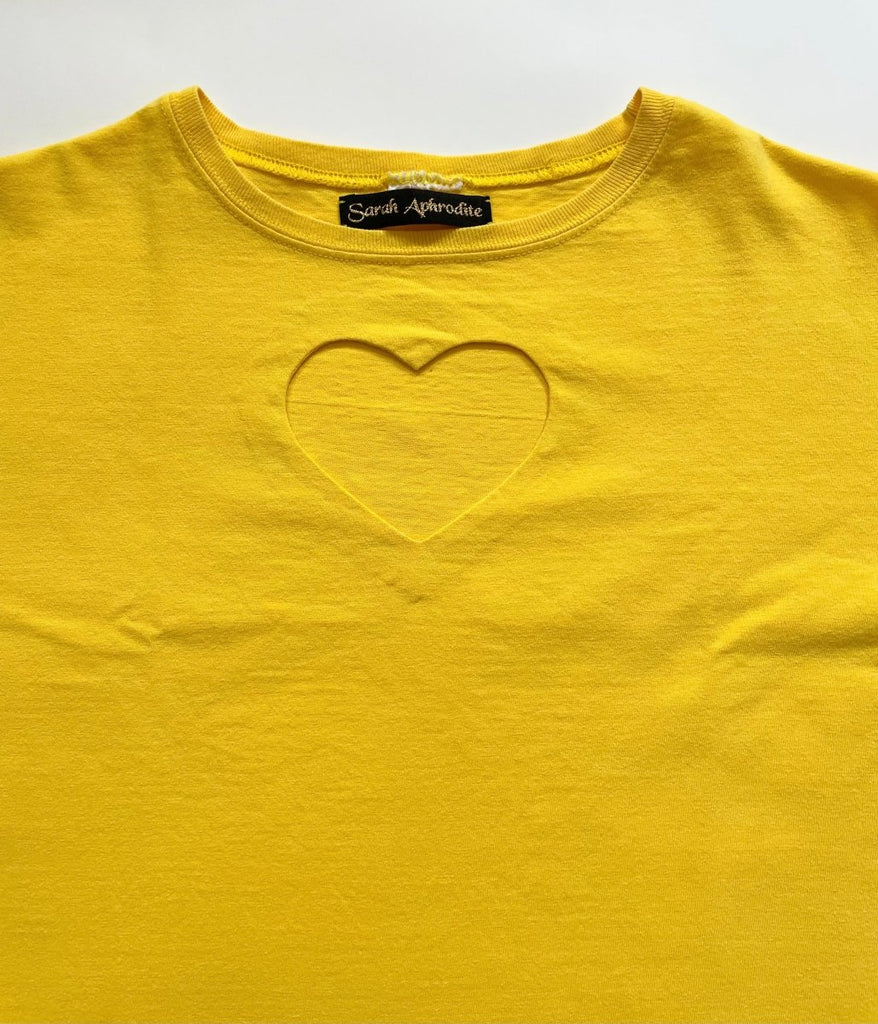 A yellow t-shirt with a heart cut-out design in the center, displayed flat on the floor.