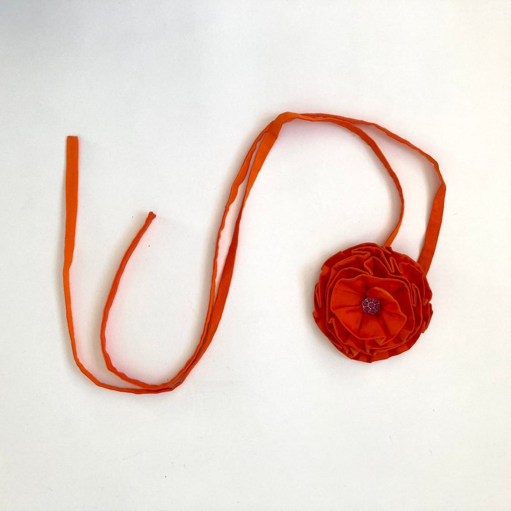 Handmade one-of-a-kind orange flower hair clip by Sarah Aphrodite, featuring a purple button gem center, silver clip, and long ties made from upcycled SA scrap fabrics.