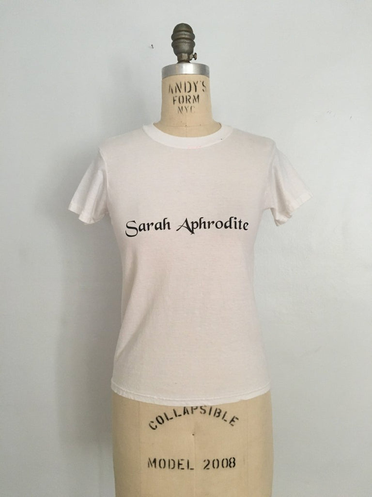 Handmade Sarah Aphrodite logo t-shirt, crafted from salvaged white cotton. Features screen-printed logo, natural markings from upcycled fabric, and a soft comfortable fit.