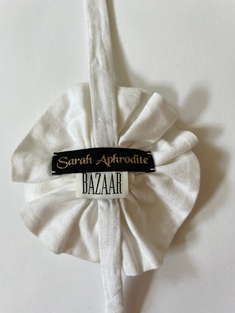 Handmade one-of-a-kind white flower accessory by Sarah Aphrodite, featuring a gold nautical button and made from upcycled SA scrap fabrics. Versatile wear as necklace, bracelet, anklet, upper arm, or garment embellishment.