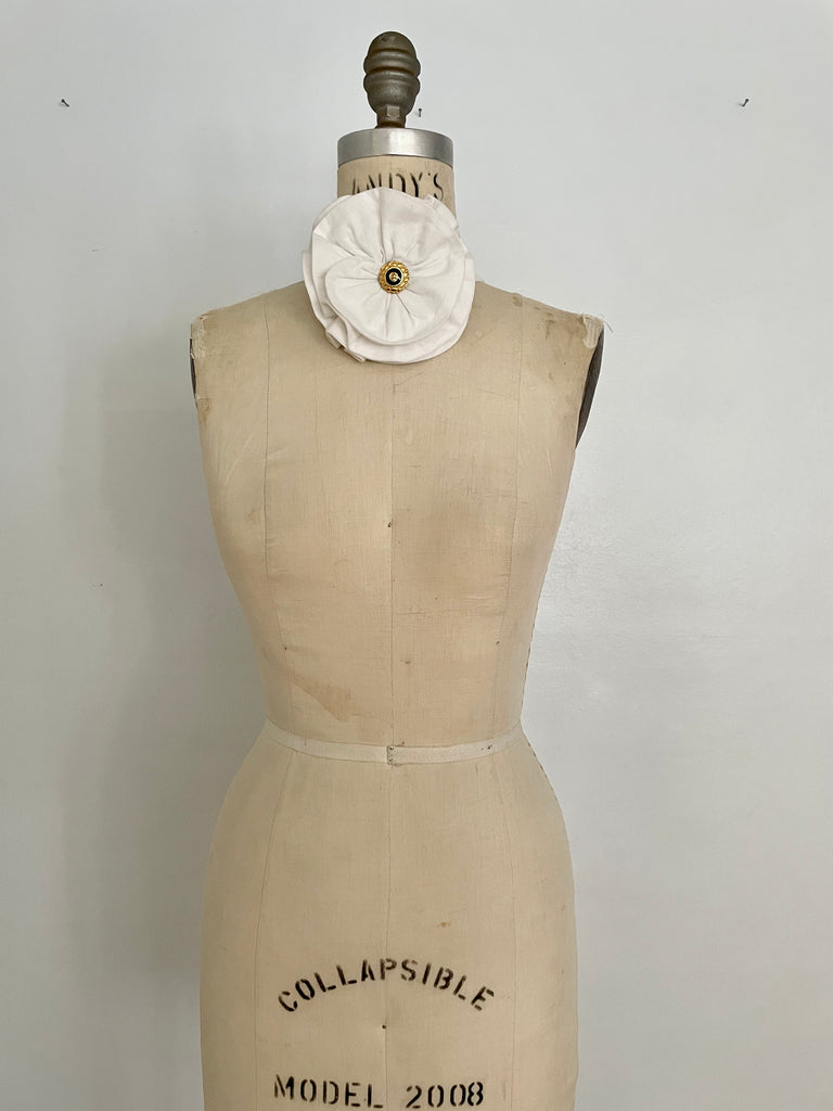 Handmade one-of-a-kind white flower accessory by Sarah Aphrodite, featuring a gold nautical button and made from upcycled SA scrap fabrics. Versatile wear as necklace, bracelet, anklet, upper arm, or garment embellishment.